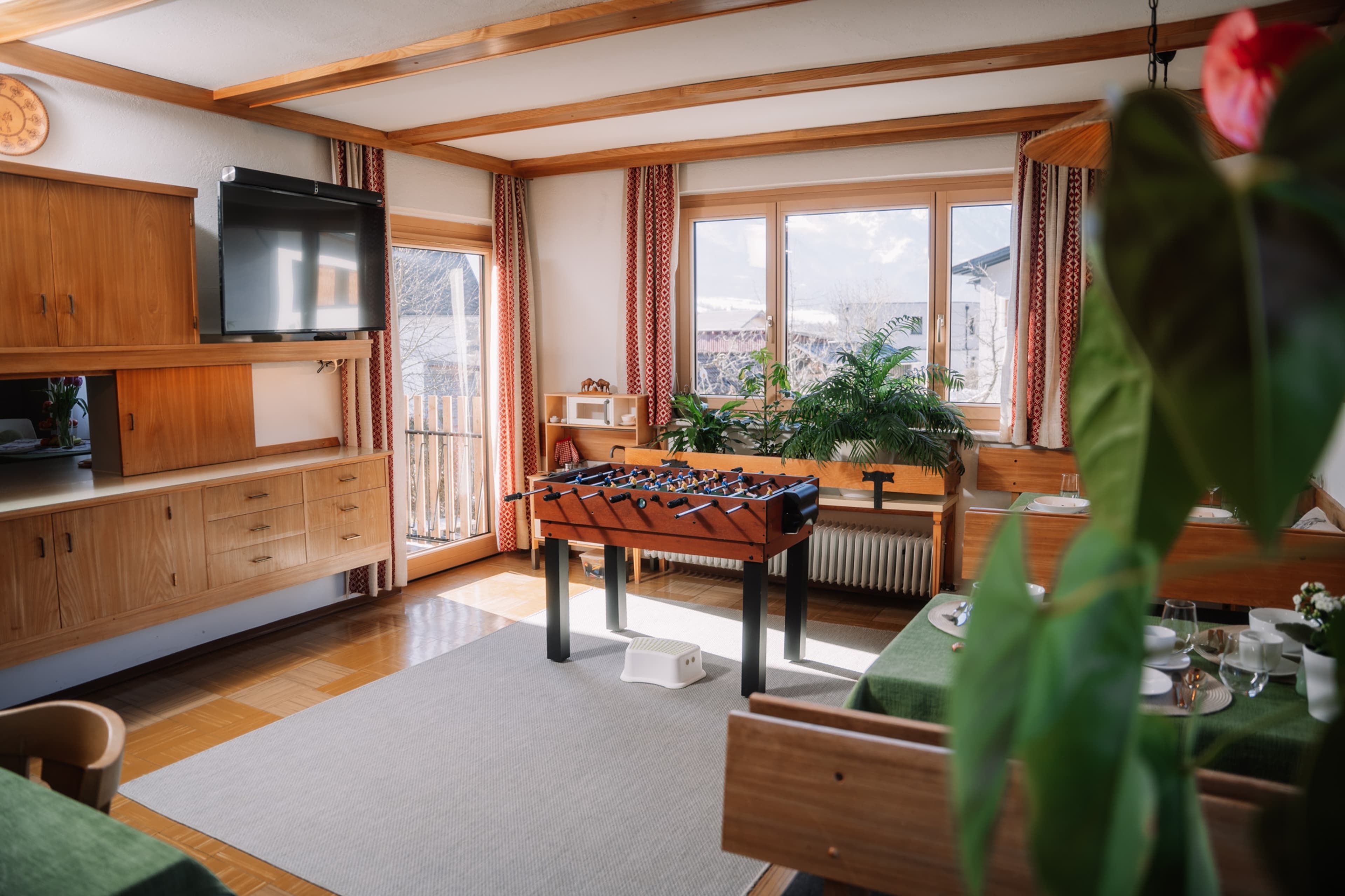 Alpenblick Gösweiner - A modern and inviting bedroom featuring a white double bed with blue and beige bedding. There are white bedside tables with black lamps. A large window with blue curtains provides natural light. On the wall above the bed hangs a scenic picture of snow-covered mountains at sunset. Wooden ceiling adds warmth.